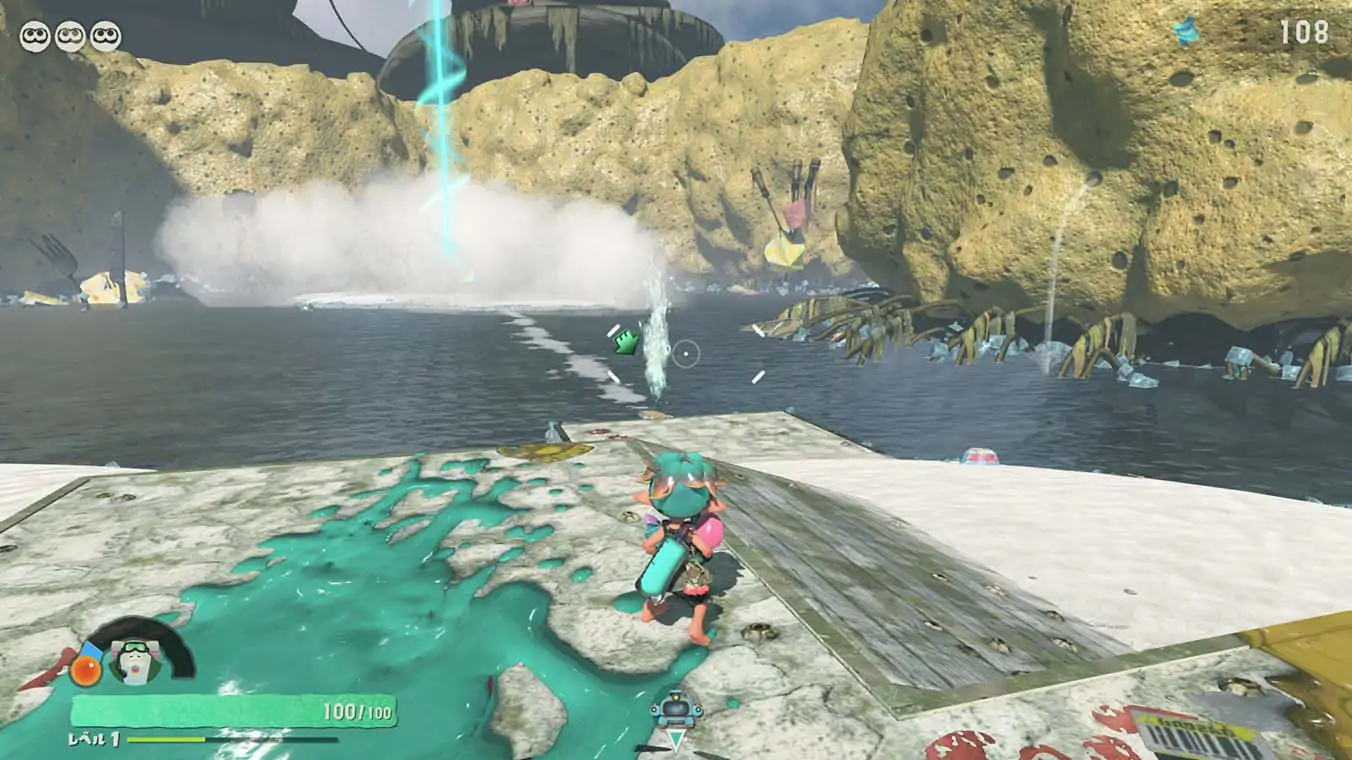 A third-person gameplay screenshot showing a character with pink and teal ink standing on a white sand bank splattered with teal ink, looking out across water toward porous, sponge-like rock cliffs.