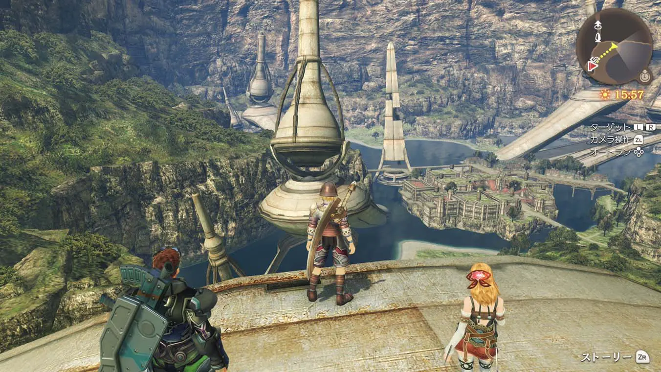 An open-world gameplay screenshot in Japanese showing three characters overlooking Colony 9 from a high metallic platform. Below them, a town with industrial, dome-shaped structures rests by a blue lake surrounded by steep, rocky canyon walls under daylight.