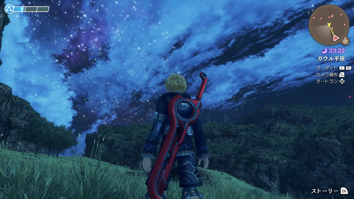 A nighttime gameplay screenshot in Japanese from a behind-the-back perspective. The protagonist Shulk stands on a grassy hill at night with a red sword strapped to his back, gazing up at a vast, vibrant blue and purple starry sky filled with constellations.